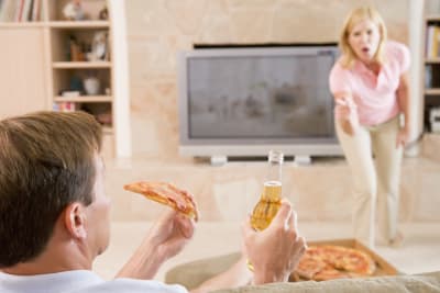 Kvinna i bakgrunden skriker åt man som äter pizza och dricker öl