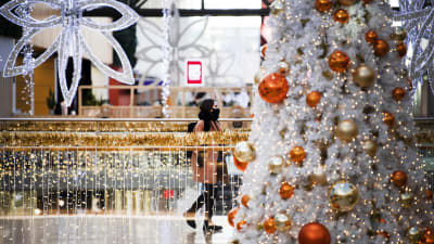 En ung person med munskydd går i ett julpyntat köpcentrum.