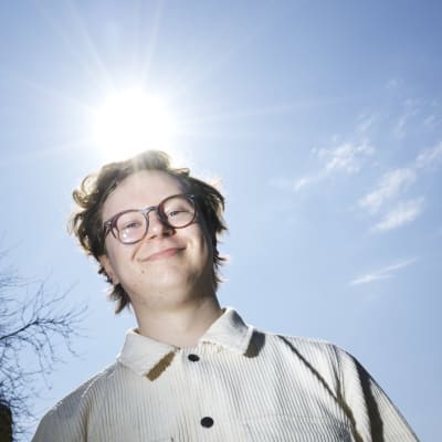 Hymyilevä mies katsoo kameraan ja aurinko paistaa selnatakana.