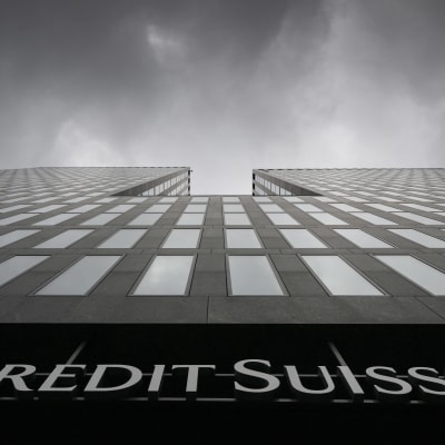 Näkymä harmaasta korkeasta liikerakennuksesta suoraan rakennuksen juurelta ylöspäin katsottuna, taivaalla harmaita pilviä ja alareunassa Credit Suissen logo.