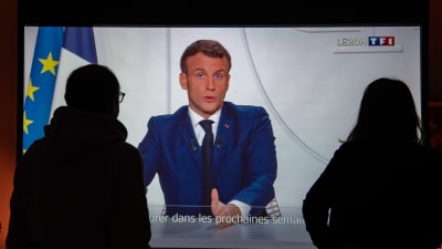 Två personer ser på en tv-skärm där Frankrikes president Emmanuel Macron håller tal.