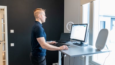 Paavo jobbar framför datorn på distans. Han har ett höj- och sänkbart skrivbord som han står invid.