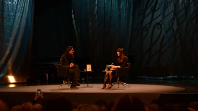 En man och en kvinna samtalar på scen.