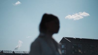 Flicka i förgrunden, i bakgrunden våningshus och himmel.
