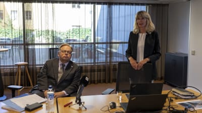 Helsingfors stads borgmästare Juhana Vartiainen sitter och personalchef Nina Gros vid ett bord. På bordet finns datorer, papper och mikrofoner.