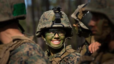 En soldat i utrustning och grönmålad i ansiktet ler.