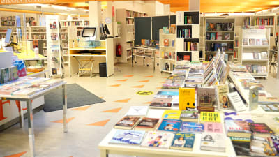 ett stort bord fullt med böcker. I bakgrunden mera böcker i bokhyllor.
