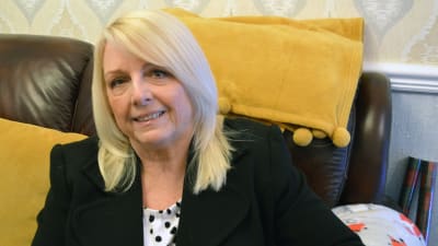 Gaynor Madgwick sitter i en skinnsoffa och ler mot kameran.