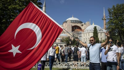 Man med turkiets flagga står utanför Hagia Sofia. I bakgrunden står flera människor.