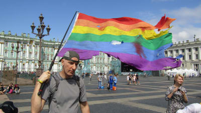 En man går med regnbågsflaggan på ett torg i Ryssland.