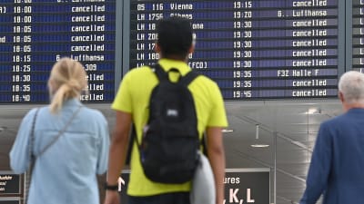 Tre personer står och tittar på en tavla på en flygplats där det står "inställt" vid många flyg.