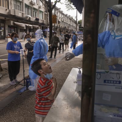 suojapukuun pukeutunut testaaja kopissa ottaa ikkunan takaa koronatestin lapsen nielusta Shanghaissa