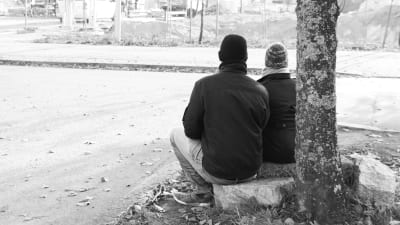 två personer sitter på gatstenar, svartvit bild