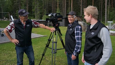 Tre män står runt en videokamera.