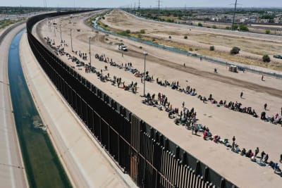 Migranter väntar längs en gränsmur för att överlämna sig till gränsmyndigheter i USA.
