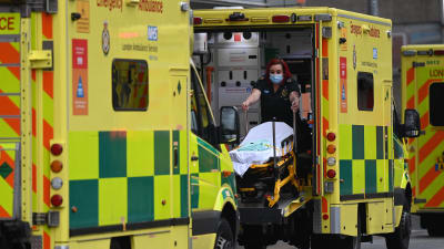 En ambulansförare rullar ut en bår ur sin ambulans framför ett sjukhus.