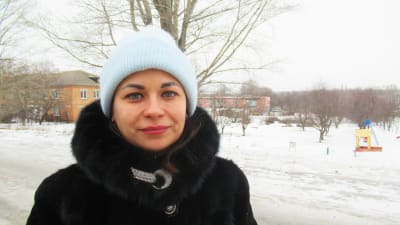 Anastasia Anizimova ser in i kameran med ett litet leende. Hon står i ett vintrigt landskap iklädd mössa och päls.