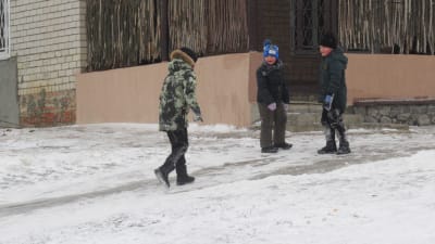 Tre barn ser glada ut på en isig gata i byn Tokaryvka.