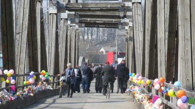 Människor promenerar och cyklar på en bro. Människor har placerat ljusa och färggranna ballonger och leksaker på båda sidor av bron.