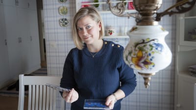Madeleine Roos i blå tröja, hemma i sitt kök, hon håller i två cd-skivor och har blont hår