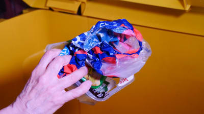 Hand som lägger plast i ett avfallskärl.