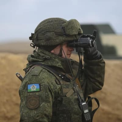 En soldat i kamouflagekläder tittar i en kikare.