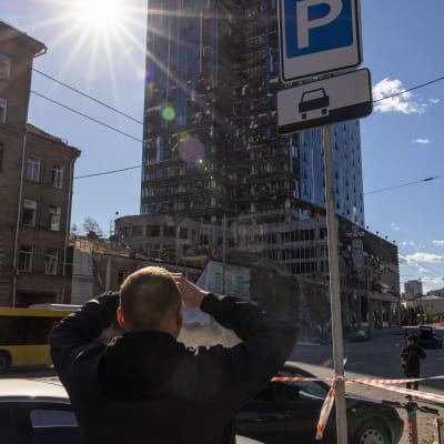 En man tittar på en skadad skyskrapa i Kievs centrum efter ryska bombningar.
