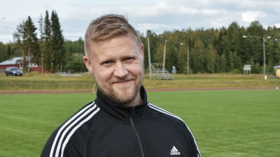 Mikael Kock iklädd sportdräkt tittar in i kameran. Idrottsplan i bakgrunden.