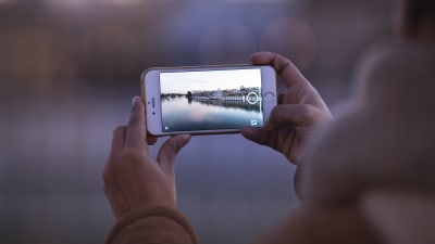 En människa håller i en mobiltelefon och tar en bild med telefonen.
