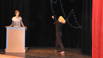 Flicka dansar på scen, kvinna står i en talarstol.