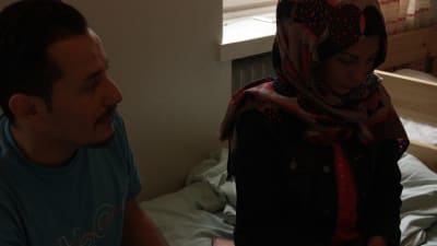 Kvinna sitter på säng i dunkelt rum,