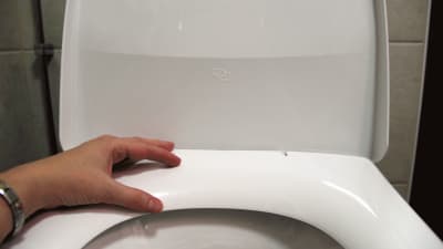 Hand som vilar mot toalettkrans.
