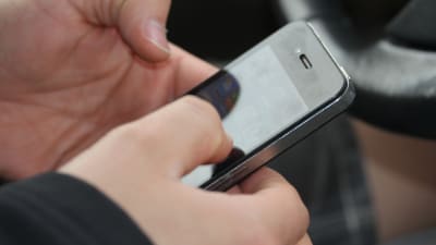 En person knappar på en smarttelefon i förarsätet på en bil.