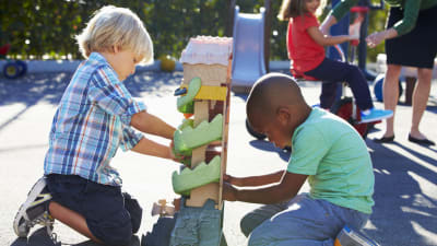 Två pojkar leker med en platsleksak på en skolgård i solen.