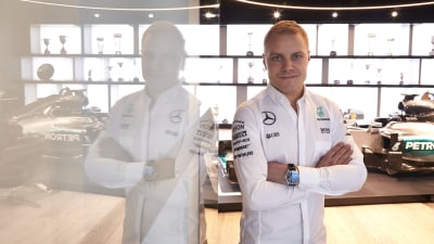 Vitklädde F1-föraren Valtteri Bottas poserar bredvid glasvägg.