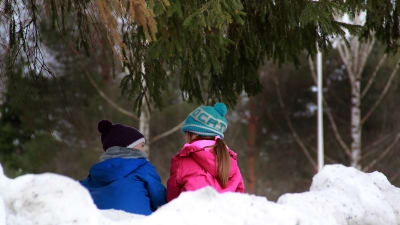 Två barn sitter i en snödrivar och pratar.