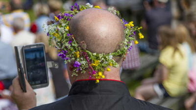 En man som har en blomkrans på huvudet och han håller i en mobiltelefon.