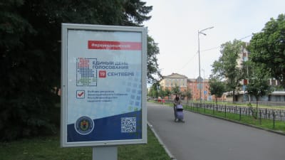 En reklamskylt som uppmanar människor att rösta i det ryska valet. Skylten finns på ett parkområde. I bakgrunden kan man se en kvinna med en barnvagn.