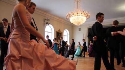 Gamlas dans i Borgå gymnasium. Flera par i kostym och klänning i skolans sal.