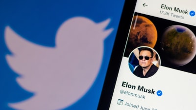 En telefon där man ser Elon Musks Twitterkonto. I bakgrunden en dator med Twitters logo på.