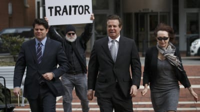 MAnafort på väg in i rättegång med frun och demonstrant i bakgrunden