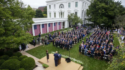 Yhdysvaltain presidentti Donald Trump puhuu tiiviisti istuvalle ihmisjoukolle Valkoisen talon pihalla.