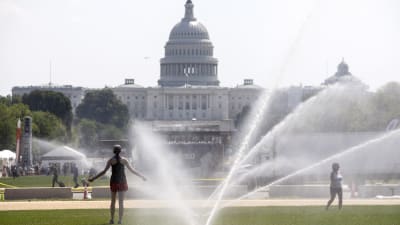 Två kvinnor svalkar sig under vattenspridare på gräsmattan framför Kapitolium i Washington DC under en extrem värmebölja i juli 2019.