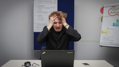 En man sitter framför en dator och river i sig i håret.