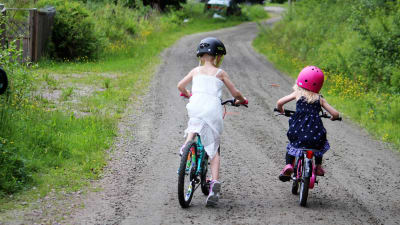två barn cyklar på grusväg