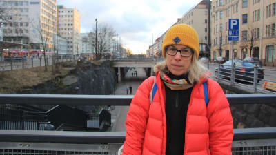 Kvinna i gul mössa och röd jacka står på en bro i centrum av Helsingfors. 
