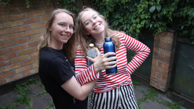Två tjejer står och ler med vattenflaskor i handen.