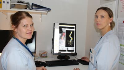 Två röntgenskötare sitter vid en dator som visar en röntgenbild på en rygg. 