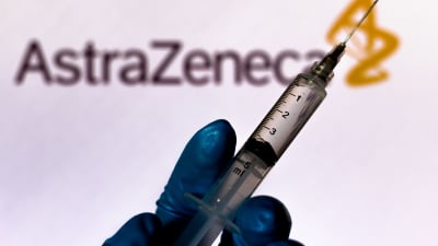 En hand håller i en spruta. I bakgrunden texten AstraZeneca.
