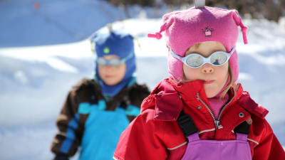 Två barn i treårsålder, ute i snön med polariserande solglasögan. 